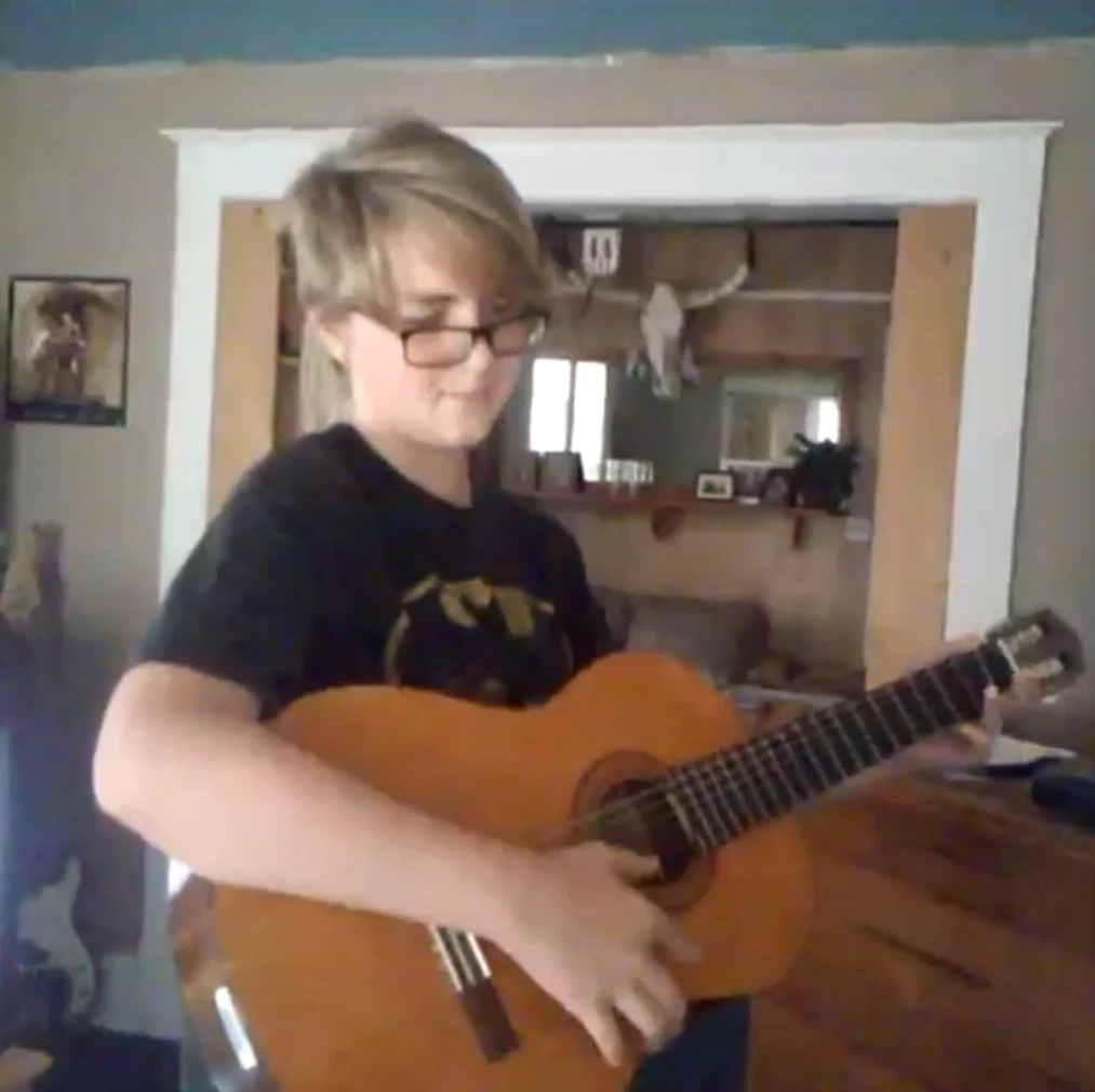 A young man with a guitar standing in his living room
