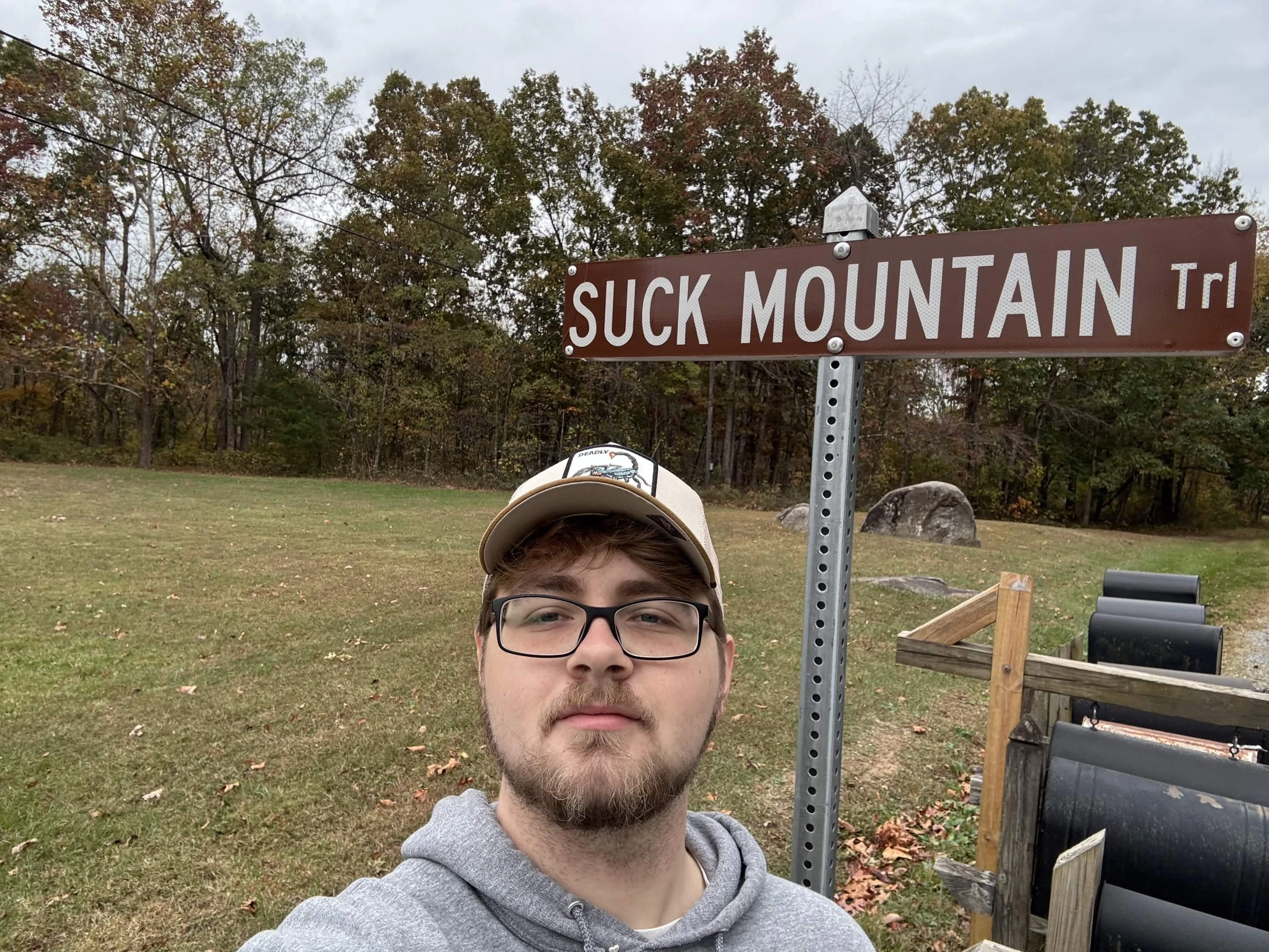 A man standing in front of a street sign that says 'Suck Mountain'